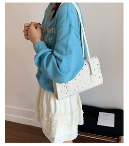 Close-up of white shoulder bag with small black heart patterns on a minimalist bench