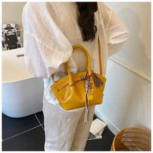 Detail of bright yellow pleated handbag with smiley charm and tassel on a model