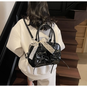 Mini zaino nero lucido con tasche a fiocco e foulard a pois su scala in legno