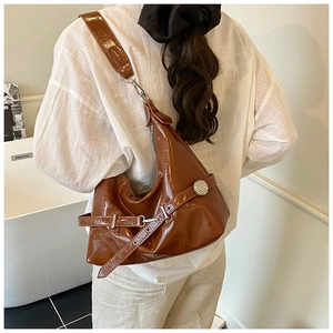Vue arrière du sac hobo en cuir verni marron brillant avec large bandoulière porté
