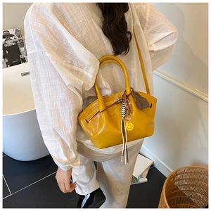 Detail of yellow minimalist dumplings bag with smiley charm on a model shoulder