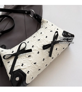 Macro shot of white embossed fabric with black bows and leather details on shoulder bag