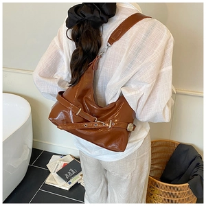 Detail of dark brown glossy patent leather shoulder bag with metallic buckle accents