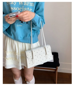 Close-up of white shoulder bag with black heart prints on a model in a casual outfit