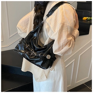 Detail of a black shiny patent leather underarm bag with silver buckle and metallic accents