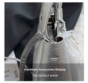 Detail of silver crocodile-embossed handbag featuring metallic buckle and lace bow charm