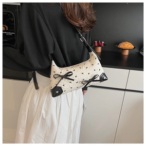 Detailed shot of white pleated shoulder bag with black leather bows on a model