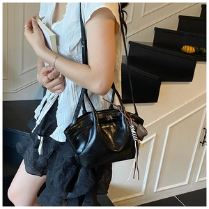 Chic black glossy leather hobo bag with metal buckle and woven tassel accessory