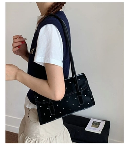 Detail of black glossy shoulder bag with white heart pattern and slim straps