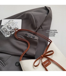 Detail of cream woven shoulder bag featuring brown leather strap and bow decoration