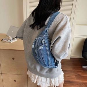Detailed back view of a blue denim crossbody bag with frayed edges and adjustable strap