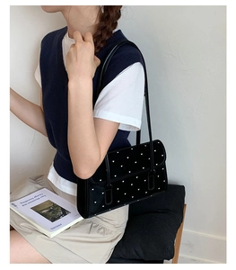 Detailed view of black velvet heart-patterned shoulder bag with long handle on a model