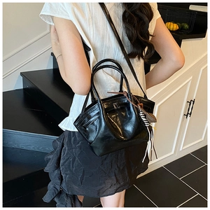 Detailed view of black glossy leather handbag with artistic pleats and decorative charms
