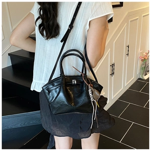 Detail of black glossy leather dumpling bag with silver buckle and woven charm