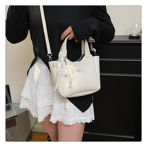 Detailed close-up of white crocodile pattern bucket bag with lace bow and pearl chain