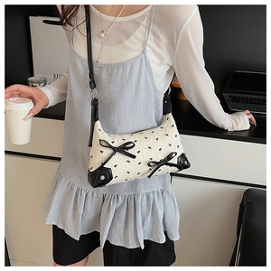 Close-up of white crescent bag with black leather bow and tiny bow prints on shoulder strap