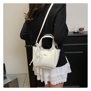Detail of cream white leather bucket bag with lace trim and elegant pearl pendant