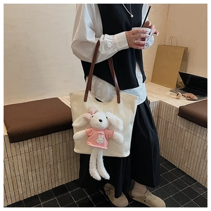 Dettaglio borsa tote in tela color crema con peluche di coniglio 3D e manici in pelle marrone