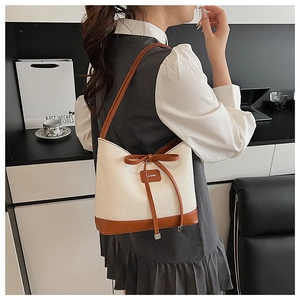 Detail of cream straw tote bag featuring brown leather trim and bow drawstring closure