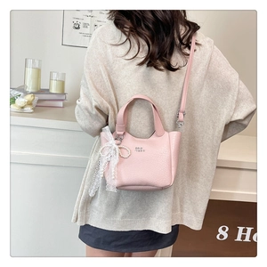 Close-up of pink lychee leather bucket bag with lace bow and pearl charm on hand strap
