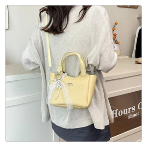 Detail of yellow leather bucket bag with white lace and pearl charm on handle