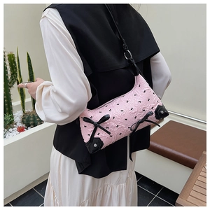 Detailed shot of pink pleated shoulder bag with black bows worn by model in minimalist setting