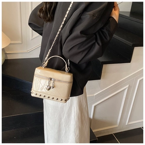 Dettaglio borsa a secchiello beige trapuntata in vernice con borchie e ciondolo a cuore