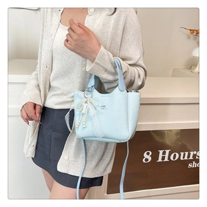 Detail of light blue mini bucket bag with leather texture and pearl lace bow charm