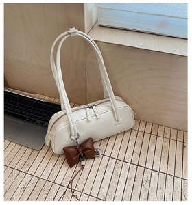 Détail d'un sac baguette crème avec un pendentif nœud en cuir marron sur un bureau
