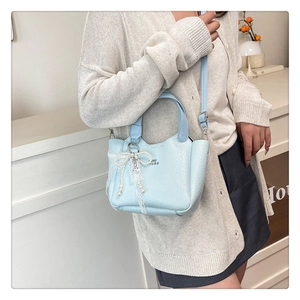 Detail of light blue bucket bag with leather texture and pearl lace bow charm