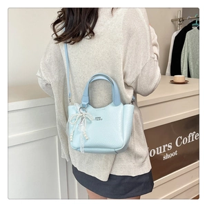 Detail of light blue textured leather bucket bag with pearl bow charm and shoulder strap