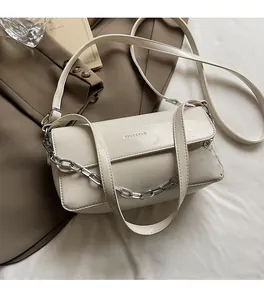Macro view of cream baguette bag featuring glossy cracked leather and silver chain detail