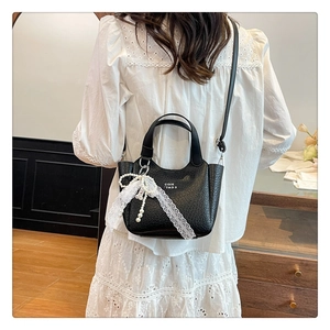 Detail of black textured bucket bag with lace bow, pearl pendant and white lettering