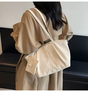 Detail of a cream-colored pleated tote bag featuring a detachable small square pouch charm