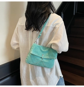 Detailed view of mint green denim crossbody bag with silver button on a fashion model