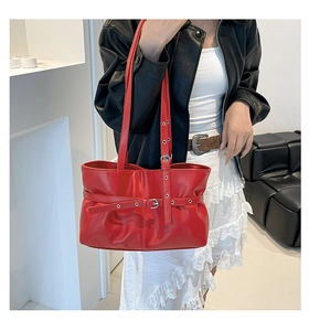 Détail du sac à bandoulière rouge avec boucle métallique et design plissé sur tenue noire