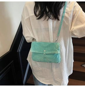 Detail view of mint green denim crossbody bag with flap and metal buckle on a model
