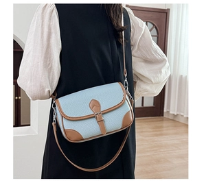 Detail of blue pebble leather crossbody bag with brown trim and metallic buckle strap