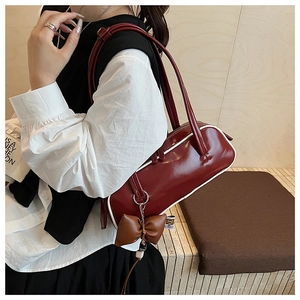 Polished red Boston bag with white trim and bow charm shown worn by a model