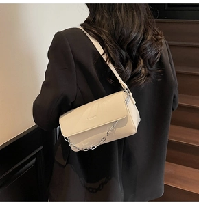 Close-up of beige baguette bag with chunky silver chain strap on a model's shoulder