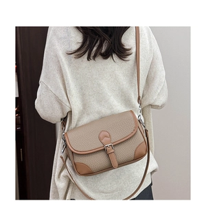 Detailed view of khaki pebbled leather shoulder bag with dark brown trim on model