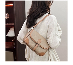 Close-up of beige leather crossbody bag with brown trim and metallic buckle detail