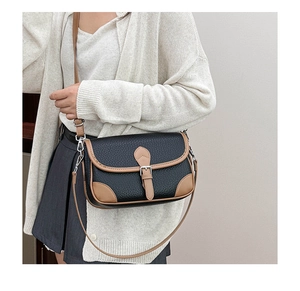 Detail of a black and brown leather crossbody saddle bag with vintage buckle on a model