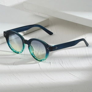 Detail einer ovalen Schildpatt-Sonnenbrille mit Metallnieten auf weißem Podest