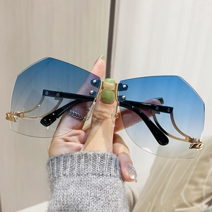 Y2K rimless sunglasses with blue gradient lenses and gold metal rivets in hand-held view