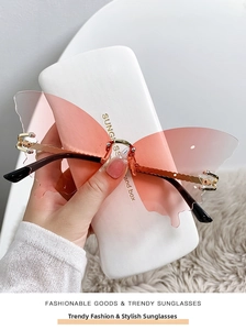 Détail de lunettes papillon sans monture avec verres dégradés roses et branches dorées