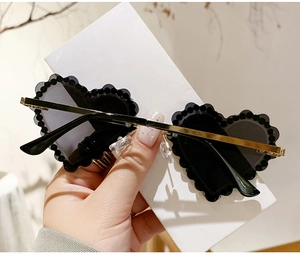 Détail de lunettes de soleil coeur sans monture avec bord perlé noir et branches dorées