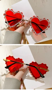Détail de lunettes de soleil coeur avec verres rouges, bordure strass et branches dorées