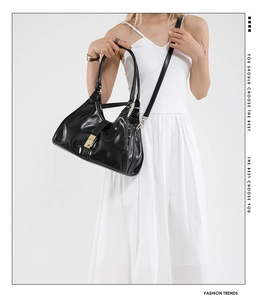 Detail showing the glossy black leather texture and gold hardware lock of this shoulder bag