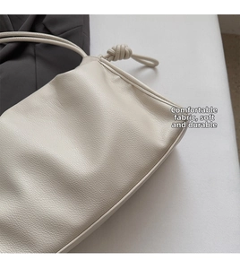 Detail of creamy white crossbody bag showing knotted strap and lychee grain leather texture